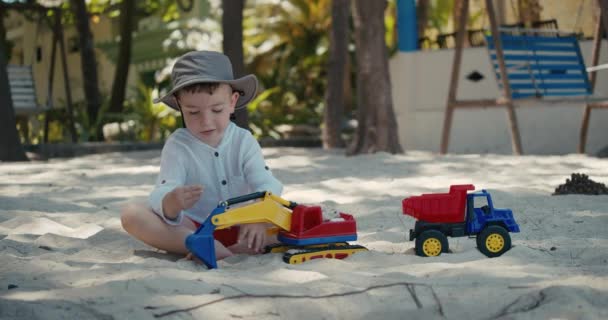 子供たちはビーチの砂の中でプラスチック製の車で遊ぶ。ビーチで砂と遊ぶ子供たちの手のクローズアップ、プラスチックのおもちゃ. — ストック動画