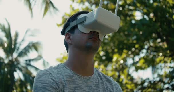 Un hombre en un casco de realidad virtual está estudiando un juego virtual. Un tipo en el parque con una camiseta gris sobre un fondo de árboles verdes se ve en gafas VR. 4K cámara lenta. — Vídeo de stock