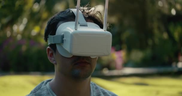 Een man met een virtual reality helm bestudeert een virtueel spel. Een man in het park in een grijs T-shirt tegen een achtergrond van groene bomen kijkt in VR bril. 4K slow motion. — Stockvideo