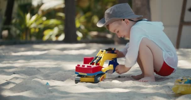 L'enfant joue avec une voiture en plastique dans le sable sur la plage. gros plan des mains des enfants jouant avec le sable sur la plage, jouets en plastique. — Video