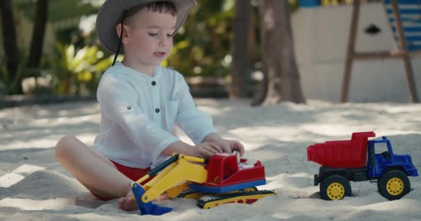 Retrato Niño bebé, lindo niño juega con un coche de plástico en la arena en la playa. primer plano de los niños manos jugando con arena en la playa, juguetes de plástico. — Vídeos de Stock