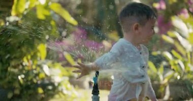 Yaz sıcağında bahçe fıskiyesiyle oynayan sevimli mutlu çocuk. Çocuk arka bahçede hortumdan su püskürterek eğleniyor. Küçük çocuk mutlu bir çocukluk geçirmiş..