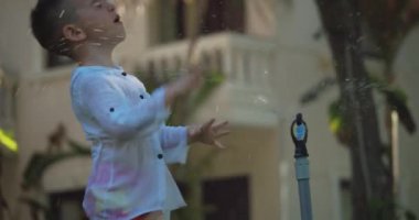 Yaz sıcağında bahçe fıskiyesiyle oynayan sevimli mutlu çocuk. Çocuk arka bahçede hortumdan su püskürterek eğleniyor. Küçük çocuk mutlu bir çocukluk geçirmiş..