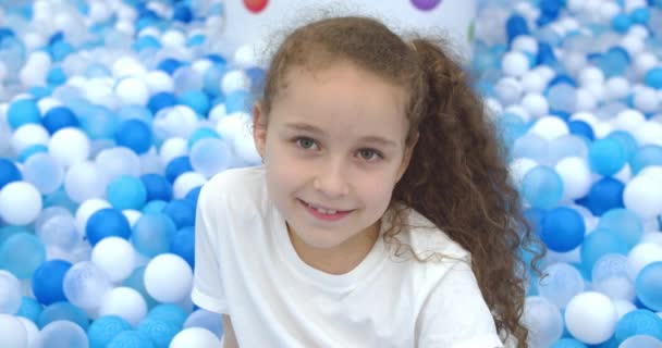 一个快乐的小女孩的画像，一个微笑的小孩，从小孩的塑料球里跳出来，小孩看着相机，一个可爱的小女孩，漂亮的脸蛋在家里玩耍，高兴极了。快乐童年的概念 — 图库视频影像