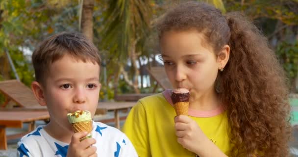 Crianças sorridentes Menino e menina felizes comendo sorvete e se divertindo olhando um para o outro. — Vídeo de Stock