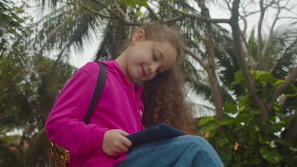 Carino bambino bambina utilizzando un dispositivo di tecnologia tablet digitale telefono o laptop. Gioca al telefono seduto sulla strada da solo. Bambini tech dipendenza concetto di gioco. — Video Stock