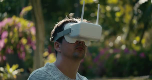 Een man met een virtual reality helm bestudeert een virtueel spel. Een man in het park in een grijs T-shirt tegen een achtergrond van groene bomen kijkt in VR bril. 4K slow motion. — Stockvideo