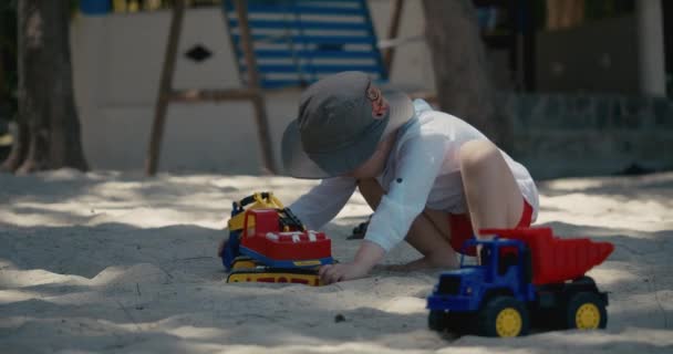 子供たちはビーチの砂の中でプラスチック製の車で遊ぶ。ビーチで砂と遊ぶ子供たちの手のクローズアップ、プラスチックのおもちゃ. — ストック動画