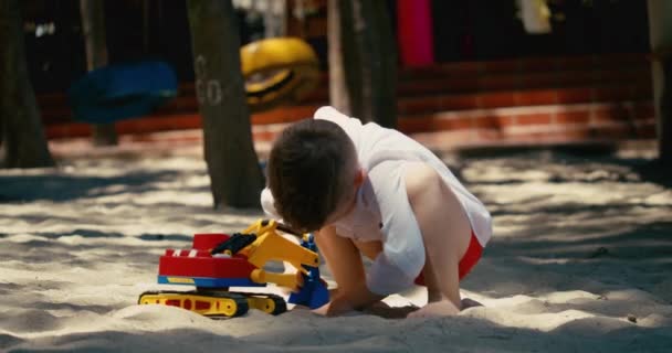 子供はビーチの砂の中でプラスチック製の車で遊ぶ。ビーチで砂と遊ぶ子供たちの手のクローズアップ、プラスチックのおもちゃ. — ストック動画