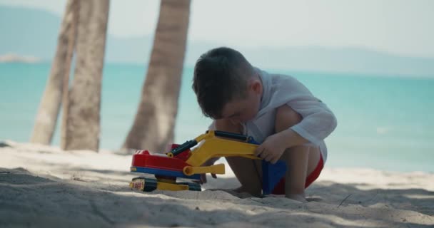 L'enfant joue avec une voiture en plastique dans le sable sur la plage. gros plan des mains des enfants jouant avec le sable sur la plage, jouets en plastique. — Video