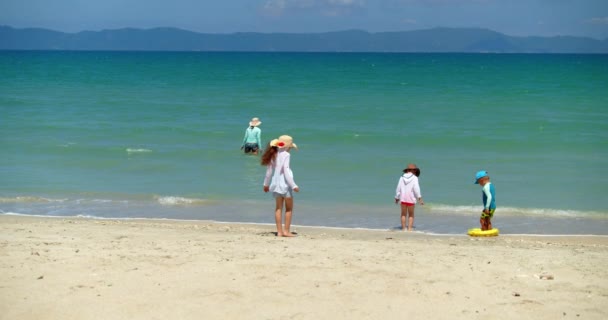 Chica divertida en un sombrero con sus hermanos en la orilla del mar está jugando, saltando, nadando, recogiendo conchas marinas, estrellas, vieiras, conchas marinas, niños en la playa junto al mar, lindos niños felices . — Vídeos de Stock