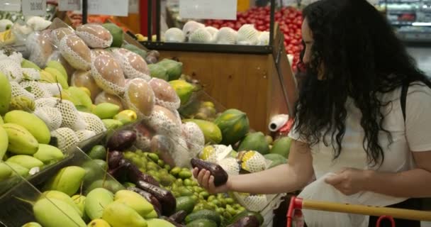 Frau macht Einkäufe im Supermarkt, gesunde Lebensmittel, Avocado legt in einen Korb, um auf einer Waage auf dem Markt, Supermarkt gewogen werden. Lebensmitteleinkaufskonzept. Auswahl der Produkte im Supermarkt