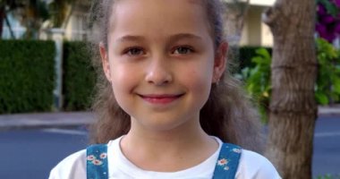 Yazın caddede duran kameraya bakan şirin bir kız çocuğu portresi. Genç, mutlu, meraklı çocuk dışarıda kameraya yakından bakıyor..