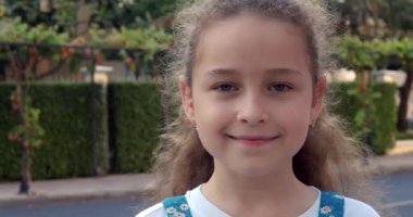 Yazın caddede duran kameraya bakan şirin bir kız çocuğu portresi. Genç, mutlu, meraklı çocuk dışarıda kameraya yakından bakıyor..