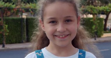 Yazın caddede duran kameraya bakan şirin bir kız çocuğu portresi. Genç, mutlu, meraklı çocuk dışarıda kameraya yakından bakıyor..