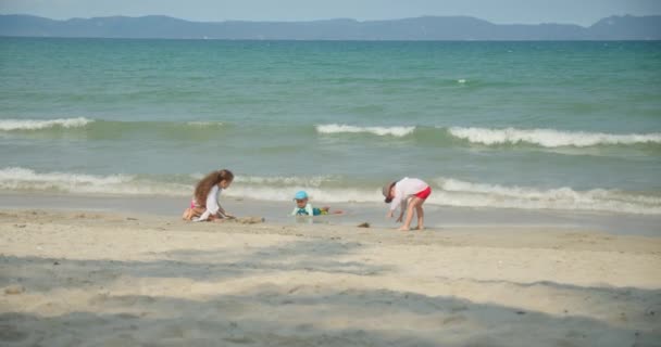 子供たちはビーチでプラスチック製のクレーンと砂の上の車で遊んでいます。ビーチで砂と遊ぶ子供や子供たちの手のクローズアップ肖像画、プラスチック製のおもちゃ. — ストック動画
