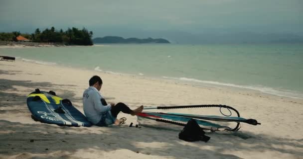 Uitzicht op het strand van de stad waar kitesurfer bereidt surfen, bereidt apparatuur voor voordat je naar zee voor windsurfing.Man controleert zeil windsurfplank voor het zeilen.Han Hoa Province, Vietnam April 3,2021 — Stockvideo