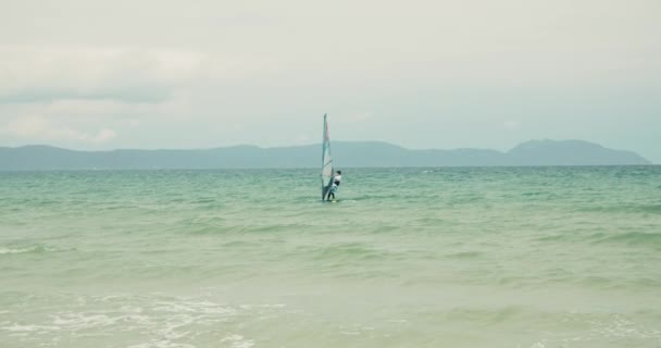 Vista de la playa de la ciudad y gente activa practicando kitesurf y windsurf. El hombre está manejando una vela de una tabla de windsurf mientras flota. Kitesurf lugar, concepto deportivo, estilo de vida saludable. — Vídeos de Stock