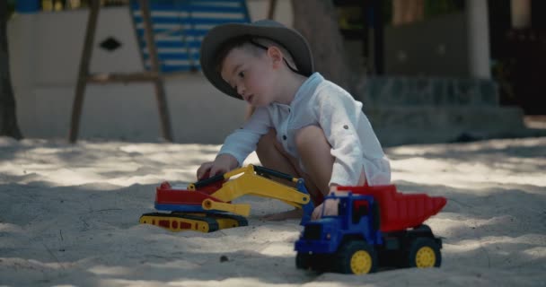 Dítě si hraje s plastovým jeřábem a autem na písku na pláži. Detailní portrét dítěte hrajícího si s pískem na pláži, plastové hračky. — Stock video