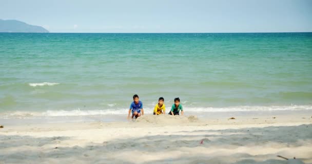 Roliga barn med vid stranden leker, småpojkar hoppar, simmar, barn på stranden vid havet, söta glada barn. Han Hoa-provinsen, Vietnam den 3 april 2021 — Stockvideo