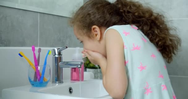 Retrato de una niña linda y feliz lavándose las manos en el baño se lava la cara sonriendo de buen humor. Cuidado diario de la salud, niña haciendo procedimientos de baño por la mañana temprano en casa. — Vídeo de stock