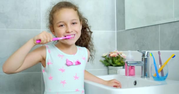 Retrato feliz lindo niño pequeño cepillándose los dientes en el baño y sonriendo. Rutina diaria de salud infantil. Niño caucásico con diente blanco mirando el espejo aislado en casa. Estilo de vida. — Vídeo de stock