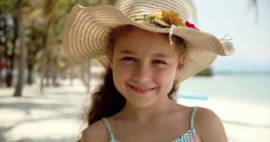 Şapkalı komik küçük bir kızın portresi, kameraya bakan gülümseyen bir çocuk, deniz kıyısında duruyor, güzel yüzlü şirin bir çocuk sahilde duruyor. Mutlu çocukluk kavramı.