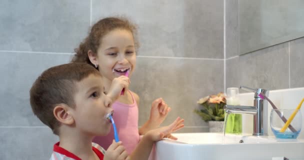 Portré boldog aranyos kisgyermekek fogmosás a fürdőszobában és mosolygós. Gyermekek napi egészségügyi rutin. Kaukázusi gyerekek, akik otthon tükröket mosnak. Életmód. — Stock videók