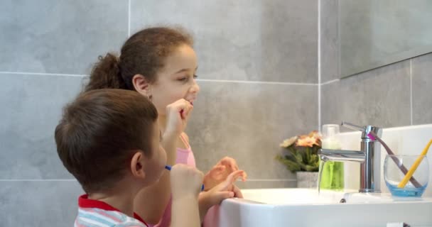 Retrato feliz bonito crianças escovando dentes no banheiro e sorrindo. rotina de cuidados de saúde diária das crianças. Miúdos caucasianos a olhar para o espelho em casa. Estilo de vida. — Vídeo de Stock