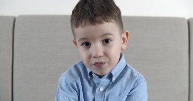 Küçük bir çocuk gördüklerinden dolayı ağzını açtı, bir çocuk şaşırmış bir yüzle kameraya baktı, evdeki kanepede oturdu, tatlı bir anaokulu öğrencisi kanepede oturuyordu. Mutlu çocukluk kavramı.