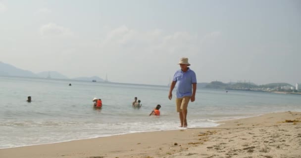 Keluarga yang sedang berlibur berenang di laut dengan anak-anak dan orang tua, orang dewasa dan anak-anak memercikkan air saat berlibur. Wisatawan laki-laki berjalan di sepanjang pasir lalu wisatawan resting.Asia, Nha Trang, Vietnam, 24 April 2021 — Stok Video