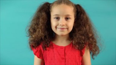 Turkuaz bir arka planda komik bir portre. Mutlu, gülümseyen küçük bir kızın kameraya bakışları. Şirin bir yüzü var, gülümsüyor, seviniyor. Mutlu çocukluk kavramı.