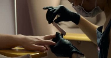 Genç kozmitolog kız bir kuaförde esmerle manikür yapıyor. Kadın kozmitolog, pedikürden önce bir hastayı tırnak törpüsüyle çivileyip hazırlıyor..