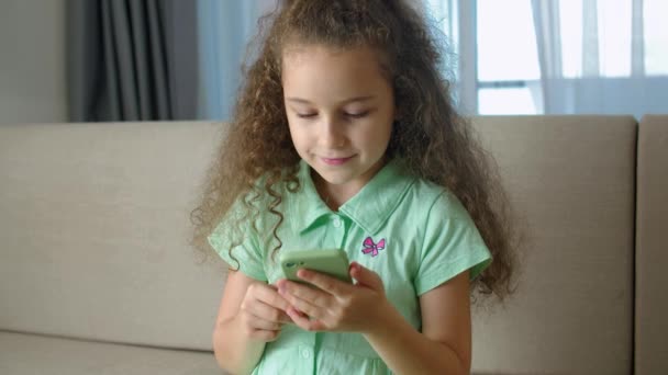 Мила дівчинка Шкільний має телефон, дитина користується смартфоном, дитина переглядає Інтернет, розмовляє по смартфону, використовує відео зв'язок вдома по телефону.. — стокове відео