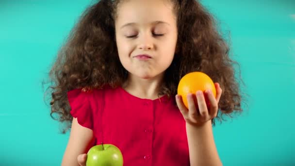 Söta barn på turkos bakgrund att hålla ett grönt äpple och apelsin och val hälsosam äta mellan frukt och apelsin. Happy Kid gör ett val för ett grönt äpple — Stockvideo