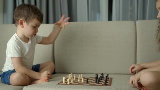 Kinder spielen Schach, während sie zu Hause auf dem Sofa sitzen, die Entwicklung des logischen Denkens bei Kindern. Entwicklung des logischen Denkens. Porträt eines klugen kleinen Jungen und einer älteren Schwester beim Schachspielen. — Stockvideo