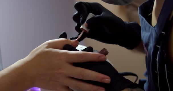 Γυναίκα αισθητικός κάνει τη διαδικασία, εφαρμόζει βερνίκι για τους πελάτες καρφί, βάφει τα νύχια μοβ. Κοσμολόγος κάνει μανικιούρ σε μελαχρινή σε κομμωτήριο.. — Αρχείο Βίντεο