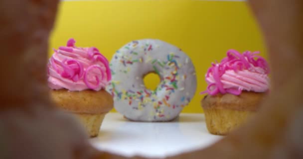 Super macro gros plan de délicieux beignets sucrés avec glaçage coloré. La caméra vole à travers le trou dans le beignet à travers deux cupcakes au beignet suivant qui se tient sur un fond jaune. — Video