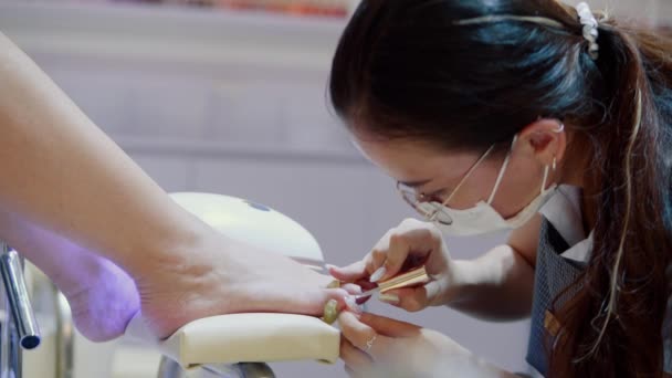Kosmetolog utför proceduren, gör penseldrag, applicerar lack, bearbetar klientens nagel med en speciell lack. Kosmitolog gör en manikyr till en kvinna i en frisörsalong. — Stockvideo