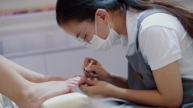 Kozmetik uzmanı işlemi gerçekleştirir, fırça darbeleri yapar, cila uygular, müşterileri özel bir cilayla çiviler. Kozmitolog kuaförde bir kadına manikür yapıyor..