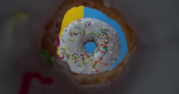 Супер макро крупным планом снимок вкусных сладких пончиков с красочной глазурью. Камера летит через дыру в пончике через два кекса к следующему пончику, который стоит на желтом фоне. — стоковое видео