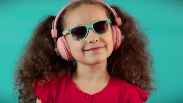 Portrait little girl headphones listening music.Cute baby listening to music on turquoise background at home. Slow motion Dance child relax with closed eyes in headphones. Cheerful carefree childhood. — Wideo stockowe