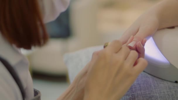 Cosmetologist in a mask performs the procedure, makes brush strokes, applies clear nail polish varnish. Cosmitologist makes a manicure to a woman in a hairdressing salon. — Stockvideo