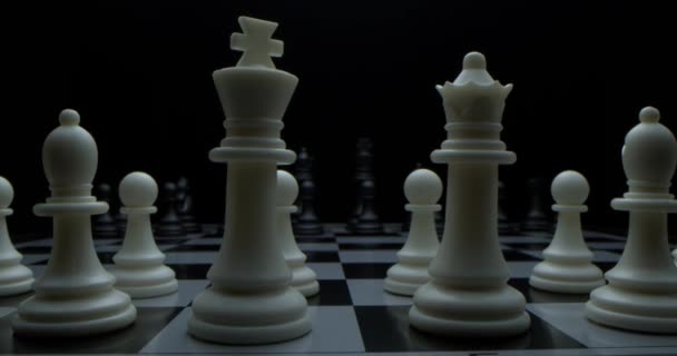 Game of chess. Filmed in a dark key. White moves with a pawn. Super-macro photography of a chessboard with chess, camera travel on a slider from white pieces to black ones. — Stock Video