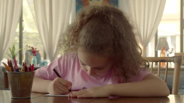 Happy Little Girl of Schattig basiskind van 7-8 jaar thuis ontspannen zit in huis en verf op papier gebruik kleurpotloden. Kind trekt, gericht kinderen basisonderwijs concept. — Stockvideo