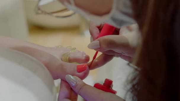 The beautician conducts the procedure, brush strokes, applies orange varnish. Cosmitologist makes a woman a pedicure in a hairdressing salon. — Vídeo de Stock