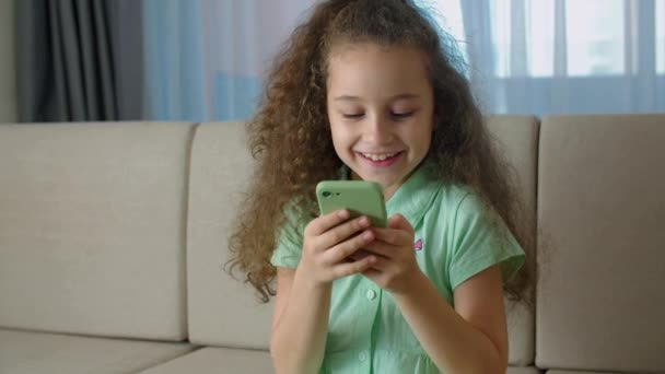 Petite fille mignonne écolier tient un téléphone, enfant utilisant un smartphone, enfant naviguant sur Internet, parlant sur un téléphone intelligent, utilise la communication vidéo à la maison sur le téléphone. — Video