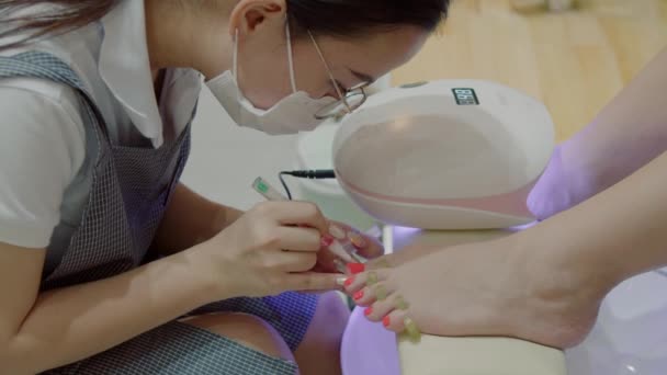Косметолог виконує процедуру, робить пензлики, наносить червоний лак. Космолог робить манікюр жінці в перукарні . — стокове відео