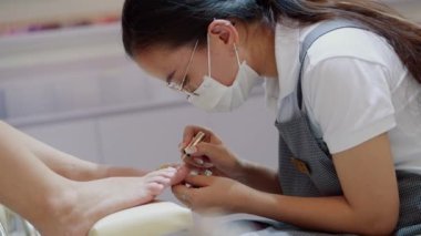 Kozmetik uzmanı prosedürü uygular, fırça darbeleri yapar, kırmızı cila uygular. Kozmitolog kuaförde bir kadına pedikür yapıyor..