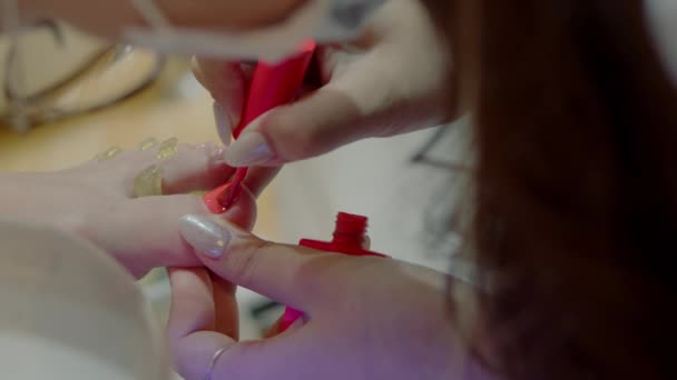 Cosmetologist executa o procedimento, faz pinceladas, aplica verniz vermelho. Cosmitologista faz uma manicure para uma mulher em um salão de cabeleireiro. — Vídeo de Stock